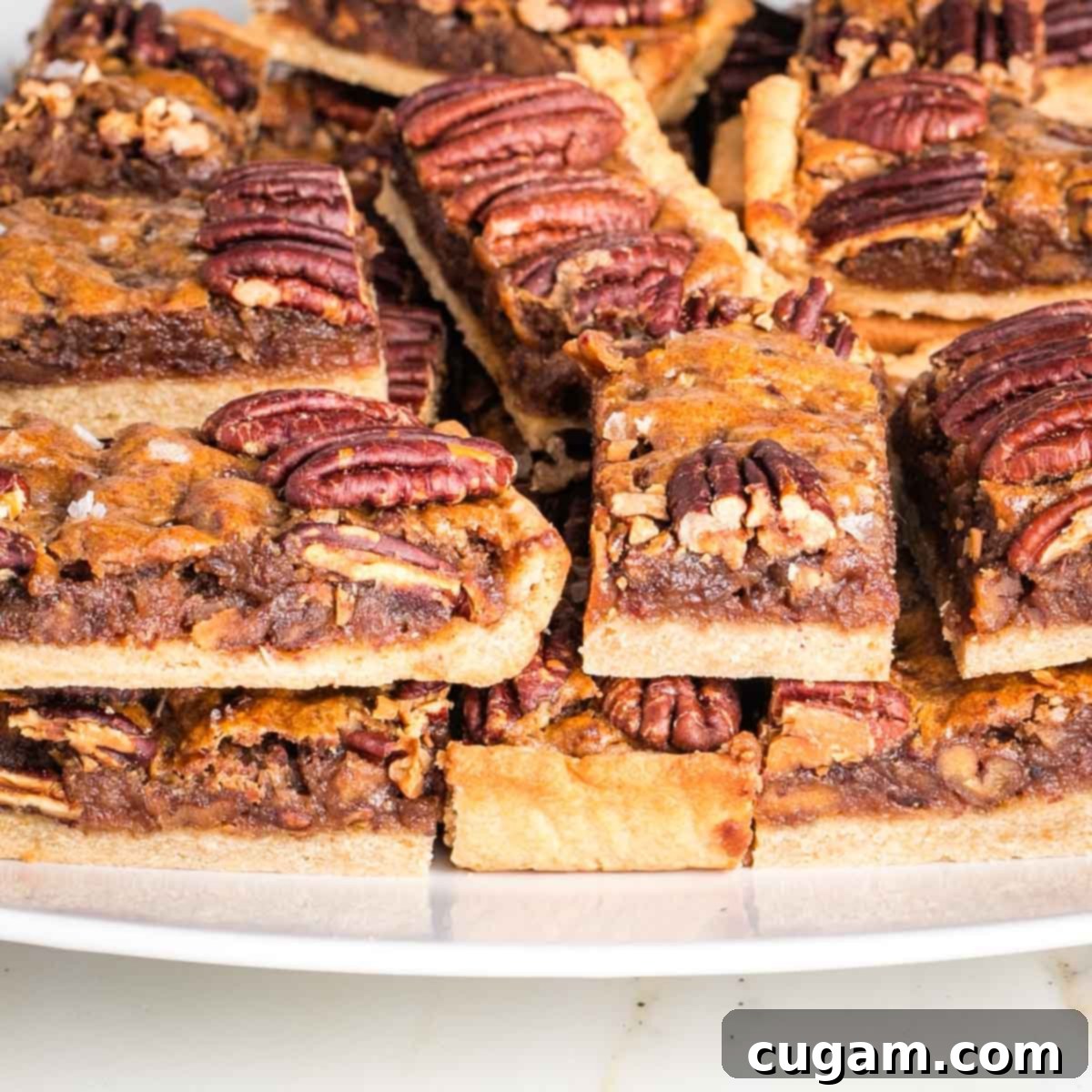 Pecan pie bars, piled on a plate, with a side view to show the three layers of pie crust, caramel filling and pecan topping. 