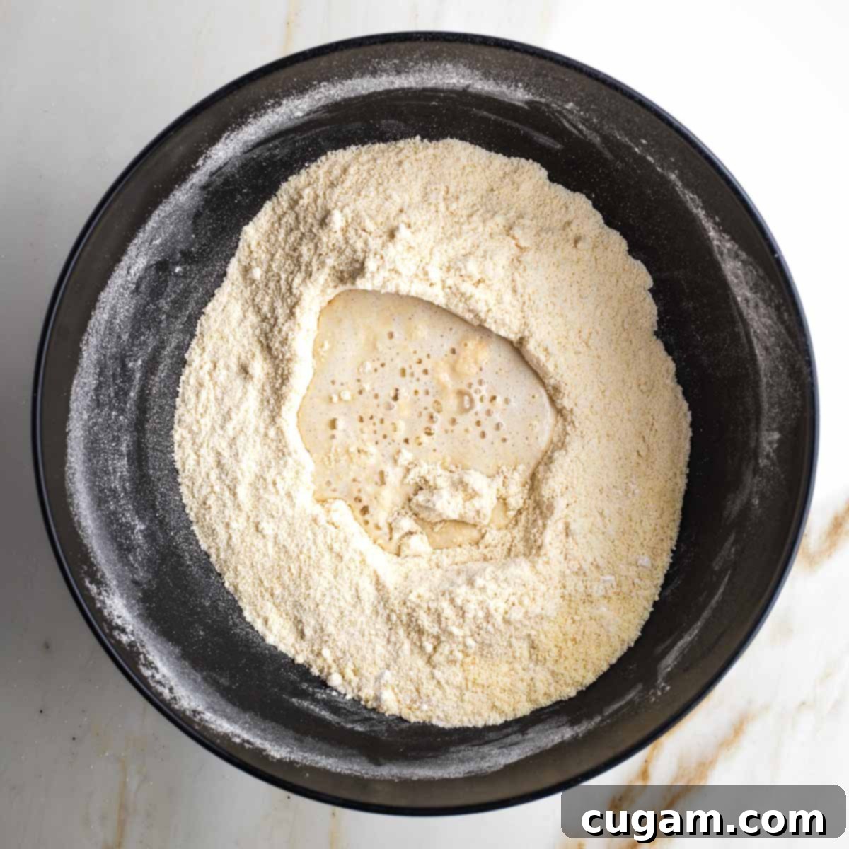 Milk mixture poured onto flour mixture in a black bowl. 