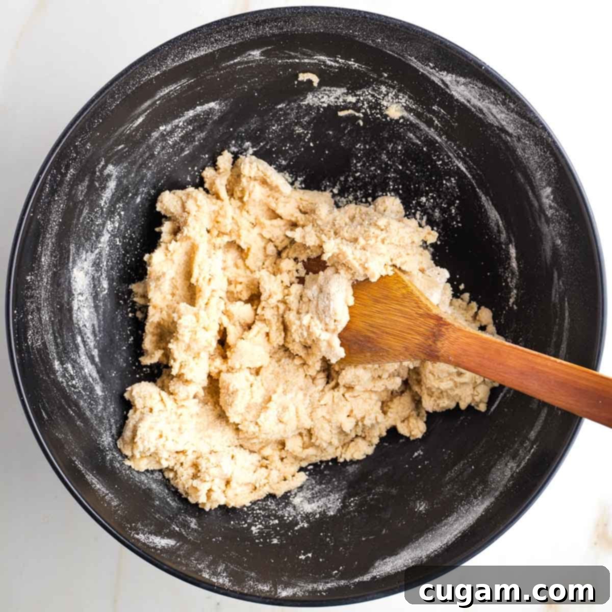 Wooden spoon stirring a dough mixture inside a black bowl. 