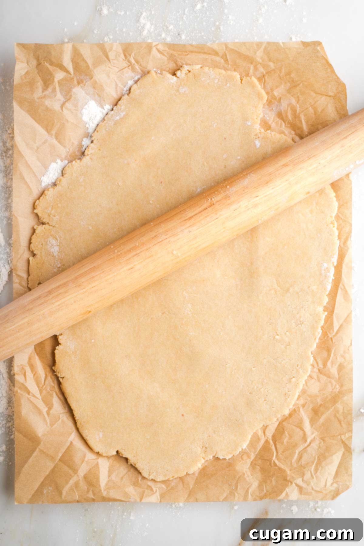 Wooden rolling pin, rolling out pie crust on a piece of unbleached parchment paper. 