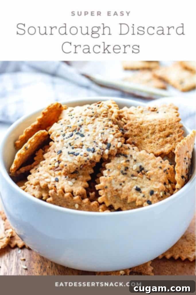 A close-up of baked sourdough discard crackers with garlic, parmesan, and everything bagel seasoning, casually arranged in a white bowl on a wooden surface.