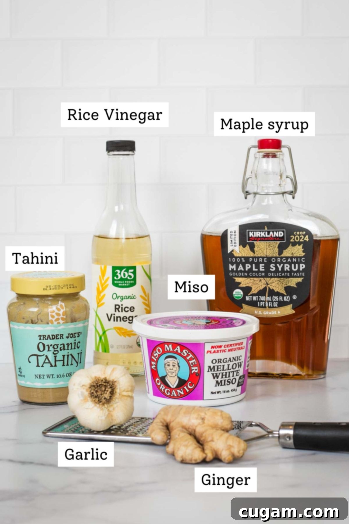 Effortless Ginger Miso Tahini Drizzle 3 Labeled ingredients for ginger miso dressing including tahini, rice vinegar, maple syrup, miso paste, fresh ginger and garlic, laid out on a table.