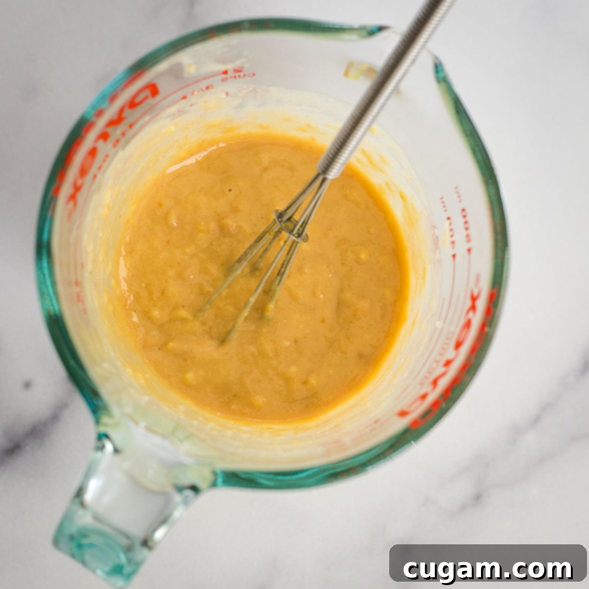 Effortless Ginger Miso Tahini Drizzle 6 Liquid measuring cup with whisk and chunky yellowish brown mixture of ginger miso dressing ingredients.