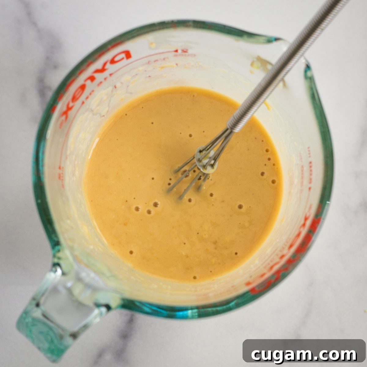 Effortless Ginger Miso Tahini Drizzle 7 Whisk in a liquid measuring cup with creamy beige ginger miso dressing, after water has been added.