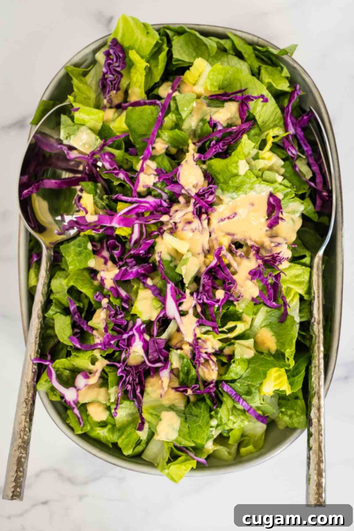 Effortless Ginger Miso Tahini Drizzle 9 Simple green salad with purple cabbage and an orange creamy ginger miso dressing drizzled on top, in a white bowl.