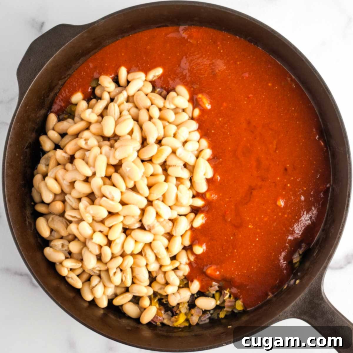 A cast iron skillet on a stovetop, filled with the aromatic sautéed vegetables, topped with rinsed canned beans and the prepared miso-infused BBQ sauce, ready for mixing.