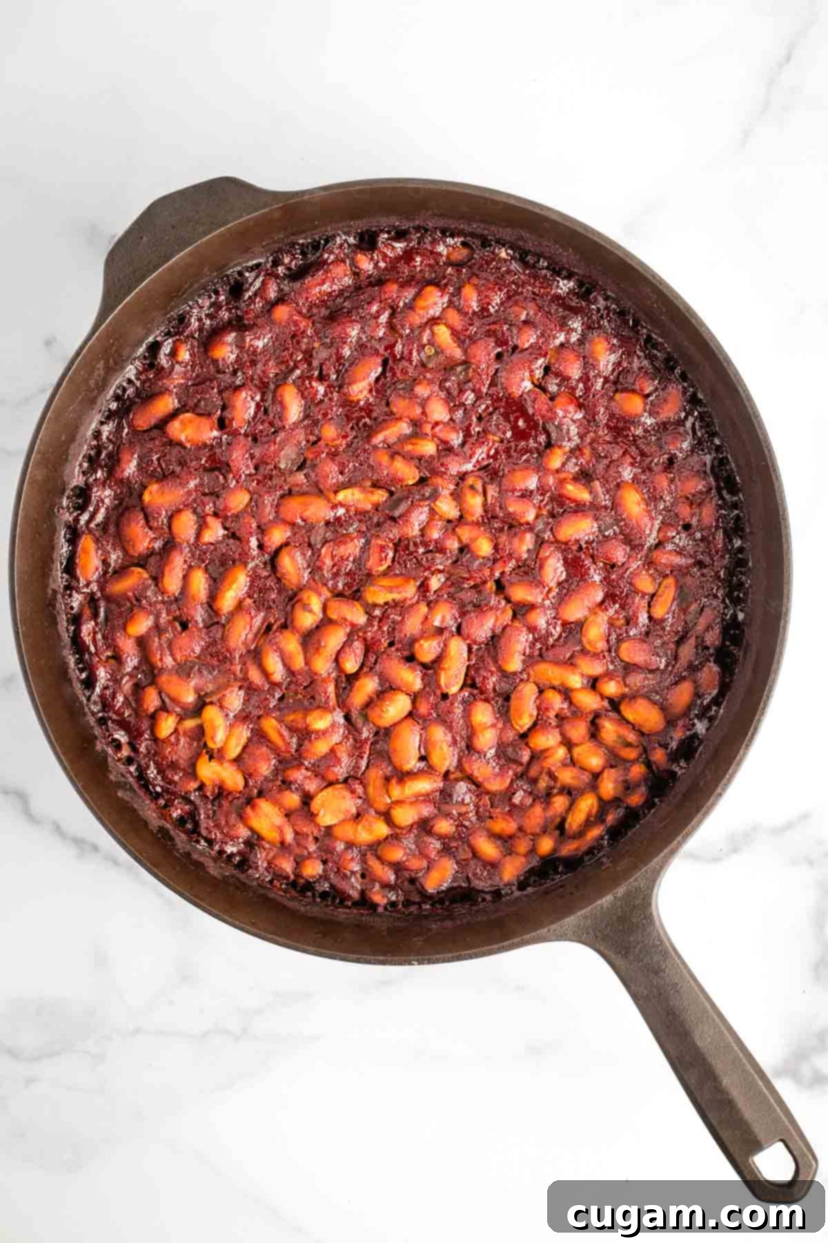A cast iron skillet filled to the brim with bubbling, rich BBQ baked beans, straight from the oven, showcasing the dish's irresistible texture and warmth.