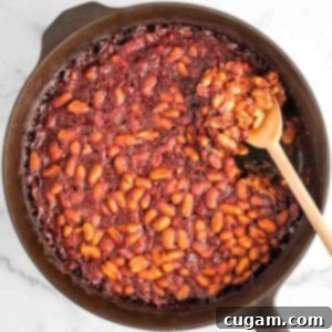 Baked beans in a cast iron skillet with wooden spoon.