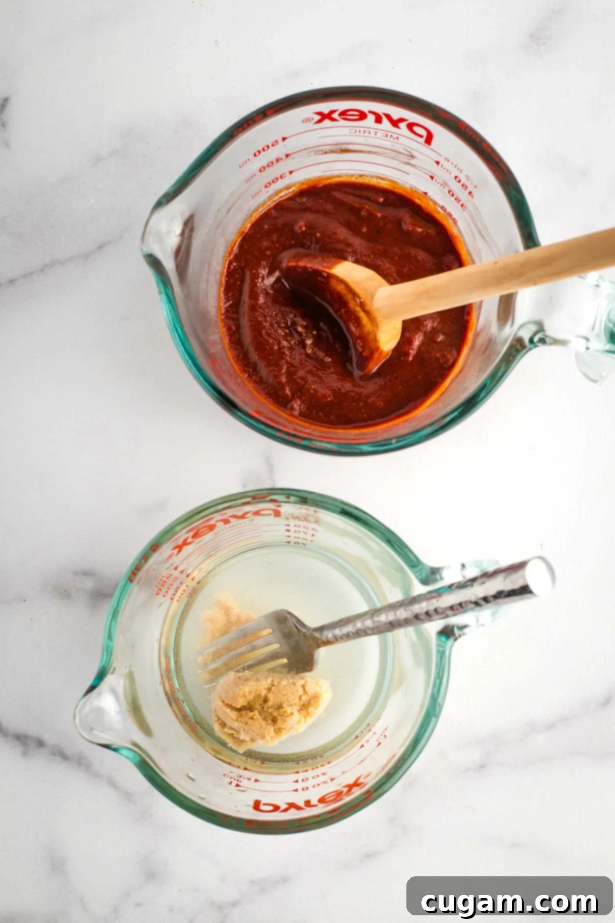 A measuring cup filled with rich homemade BBQ sauce, with a separate small measuring cup containing miso paste diluted in water, ready to be combined.