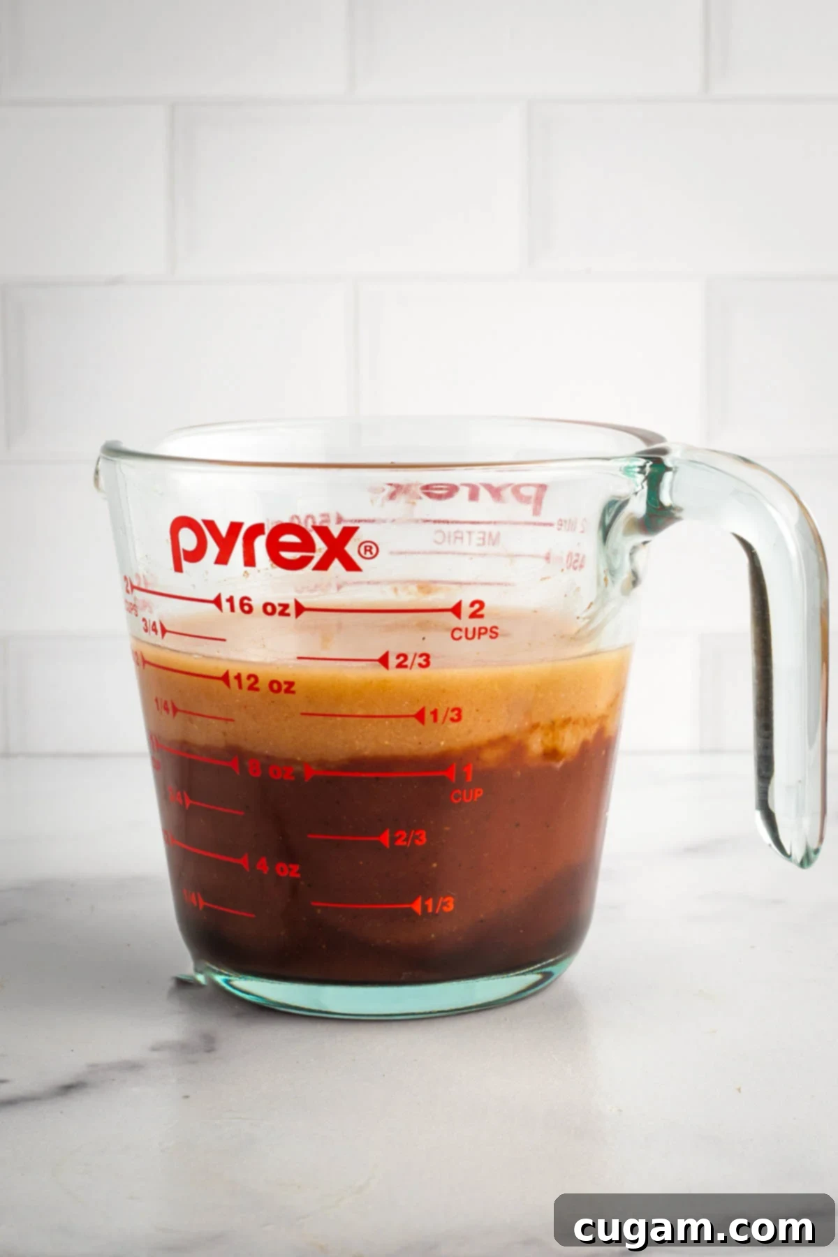 A measuring cup with BBQ sauce at the bottom, topped with the recently diluted miso paste, ready to be stirred and fully incorporated for the baked beans.