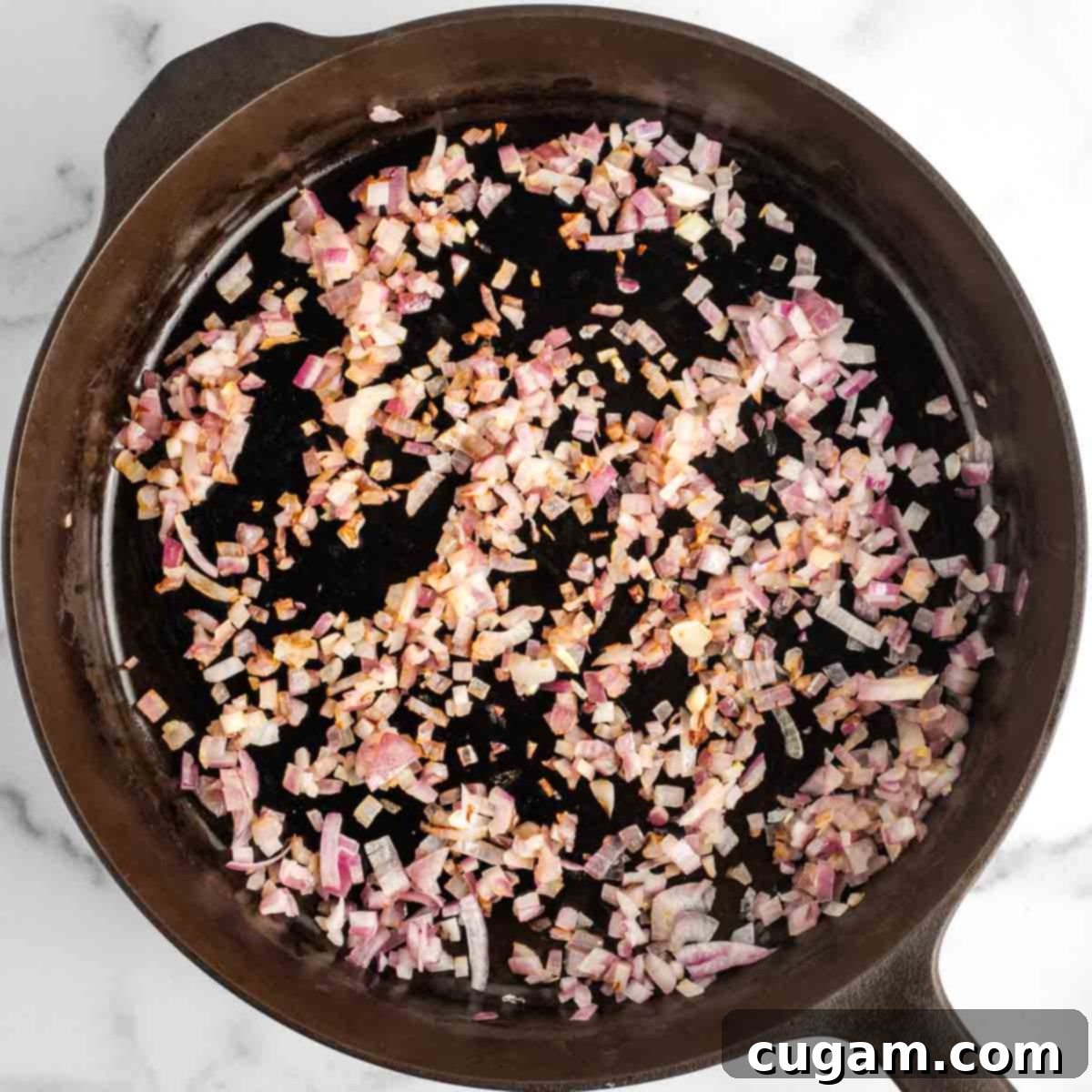 A cast iron skillet on a stovetop, filled with beautifully sautéed diced red onion, glistening and tender, ready for the next steps in the baked beans recipe.