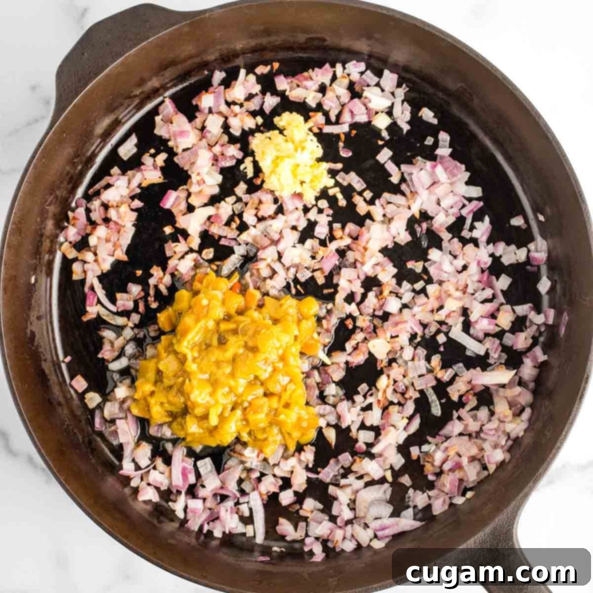 Sautéed diced red onions in a cast iron skillet, now joined by finely minced garlic and diced green chiles (including their liquid), creating an aromatic base for the baked beans.