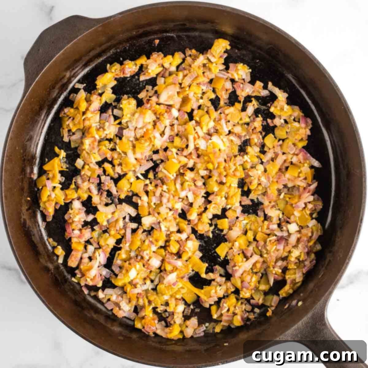 A close-up of a cast iron skillet with perfectly sautéed onions, fragrant minced garlic, and diced green chiles, forming a beautiful, golden base for the delicious baked beans.