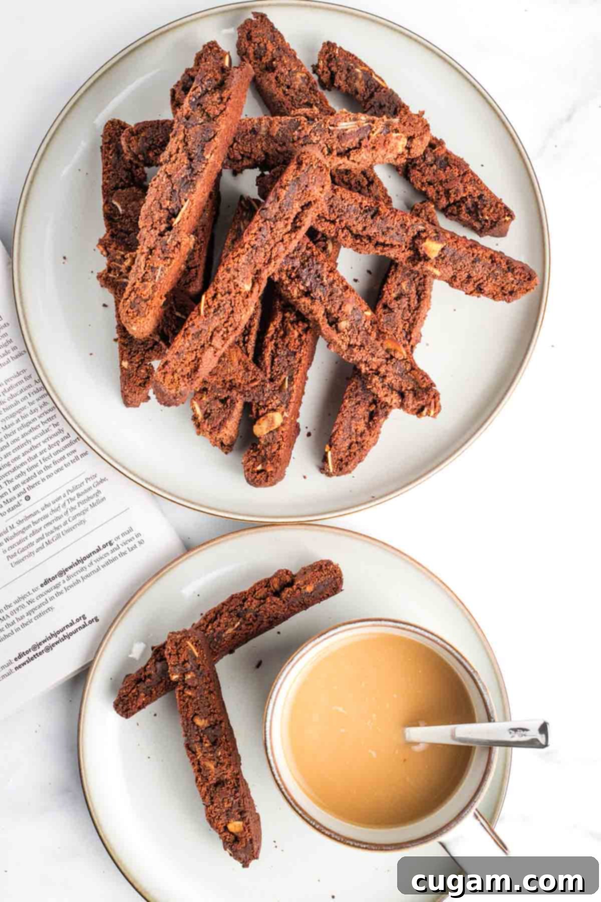A plate piled high with golden-brown chocolate almond biscotti, with a smaller plate holding two biscotti and a cup of coffee nearby, inviting a cozy snack time.