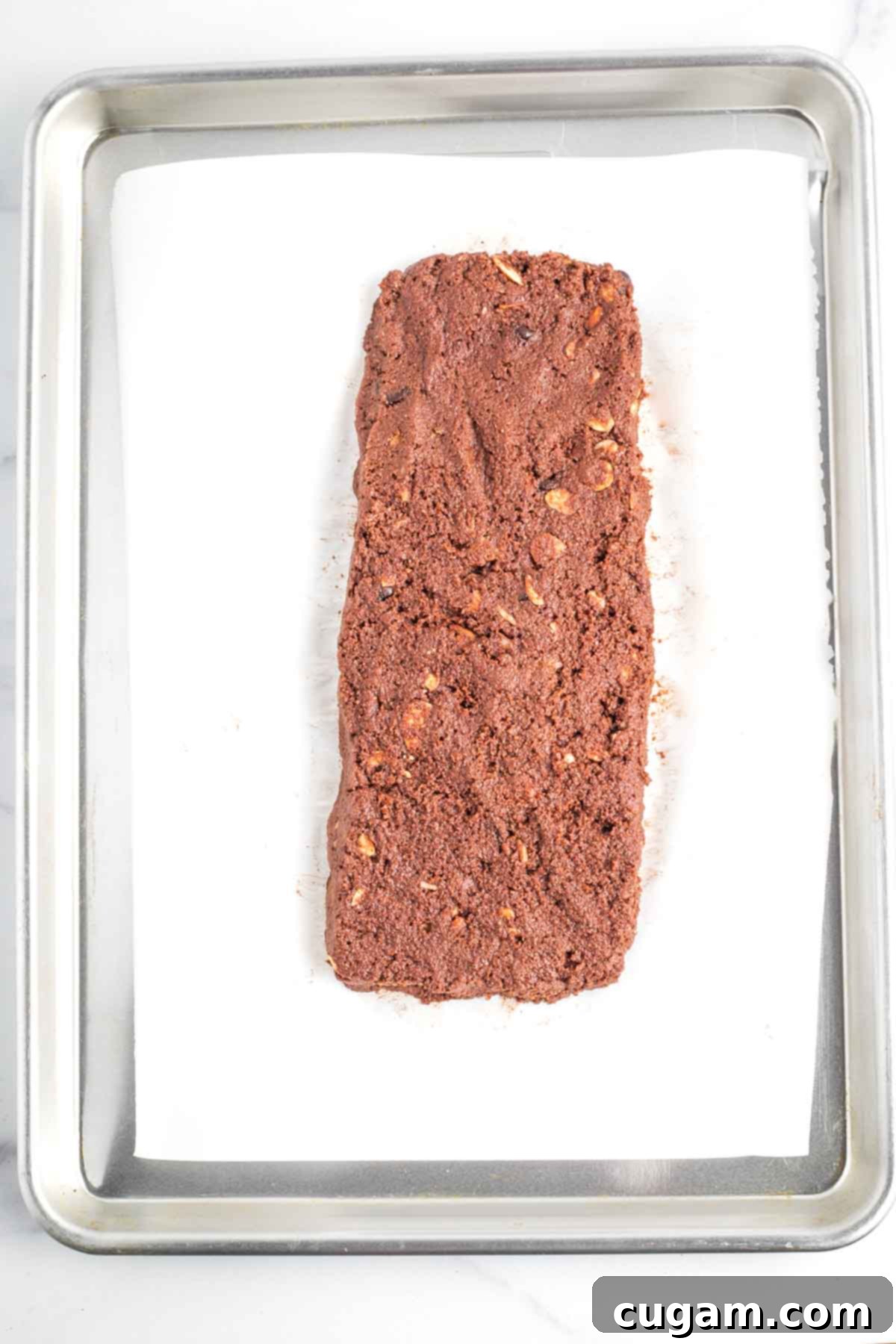 Hands shaping the chocolate biscotti dough into an even log on a baking sheet, preparing it for the first bake.