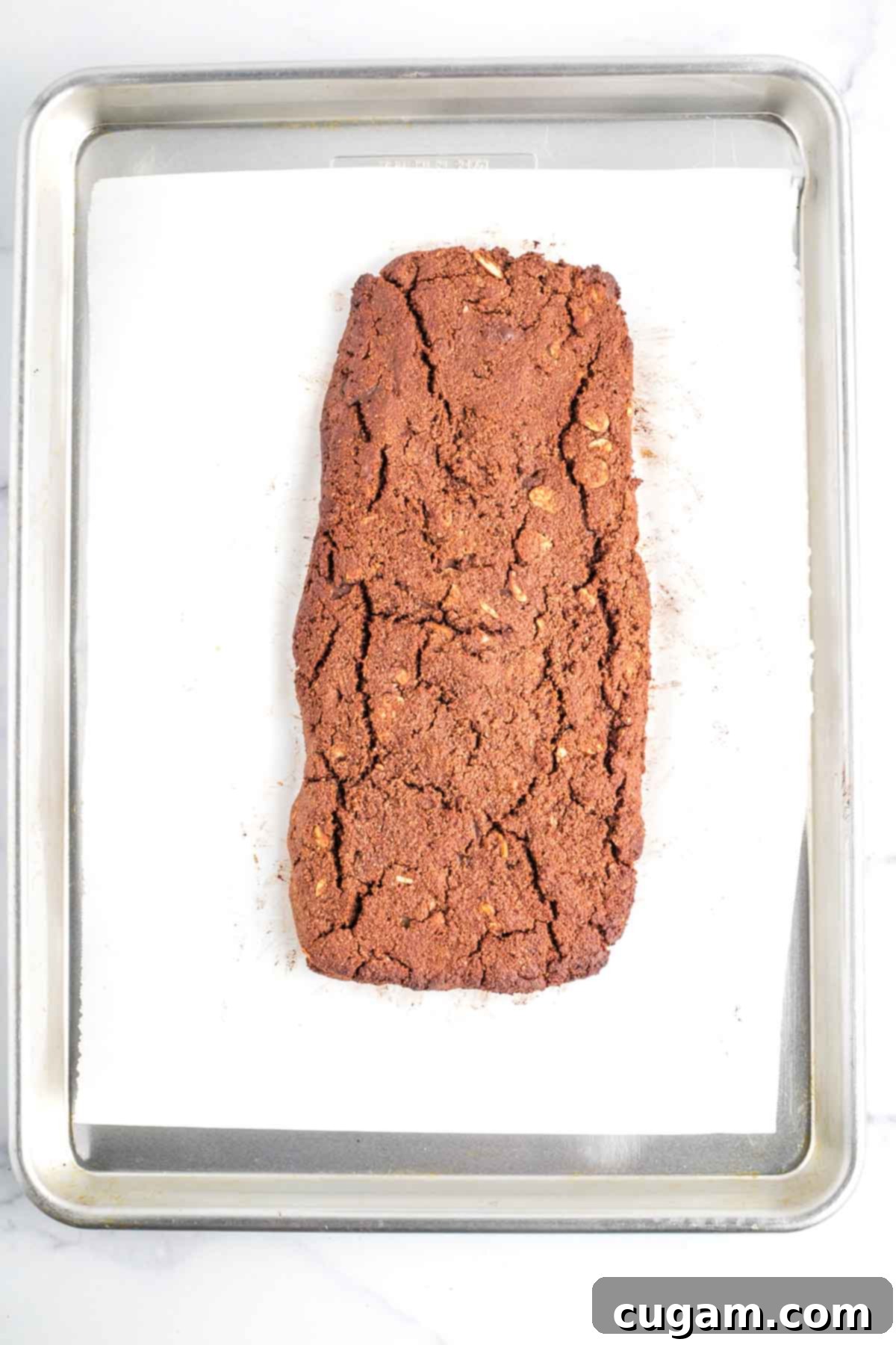 A perfectly baked loaf of chocolate biscotti, showing a slight crack on the top, indicating readiness for slicing.