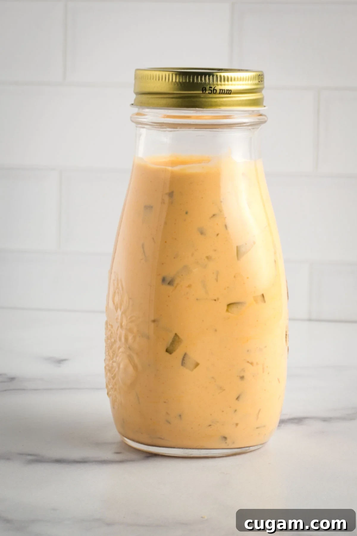Small bottle of homemade vegan special sauce for burgers, with a vibrant orange hue and visible pickle bits.