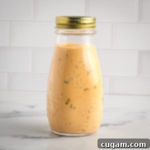 Bottle of orange-hued burger sauce with visible bits of chopped pickles.