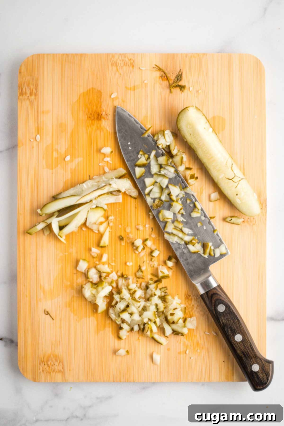 Finely dicing dill pickle spears into small cubes on a wooden cutting board.