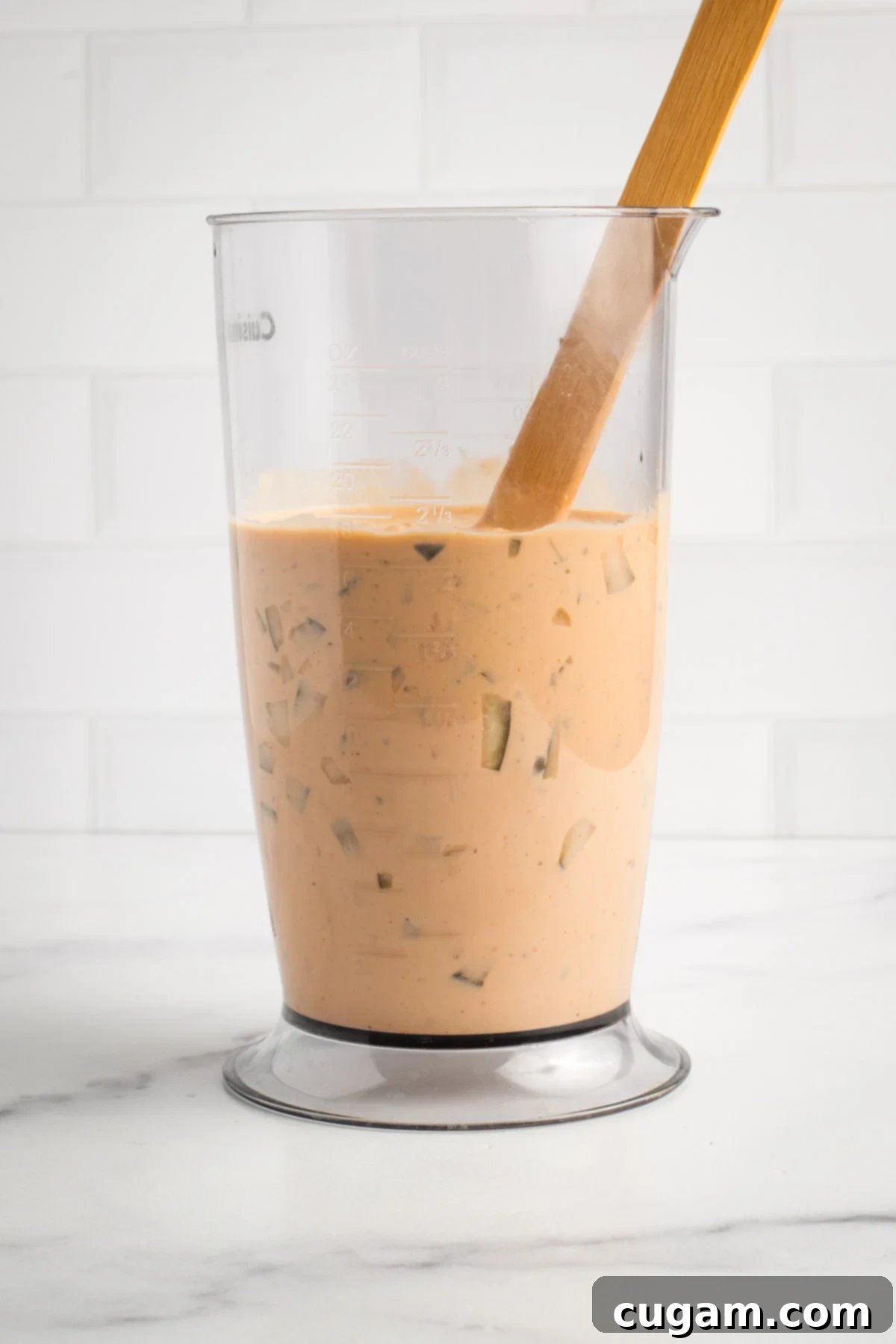 Stirring the diced pickles into the peach-colored burger sauce with a spoon to ensure even distribution.