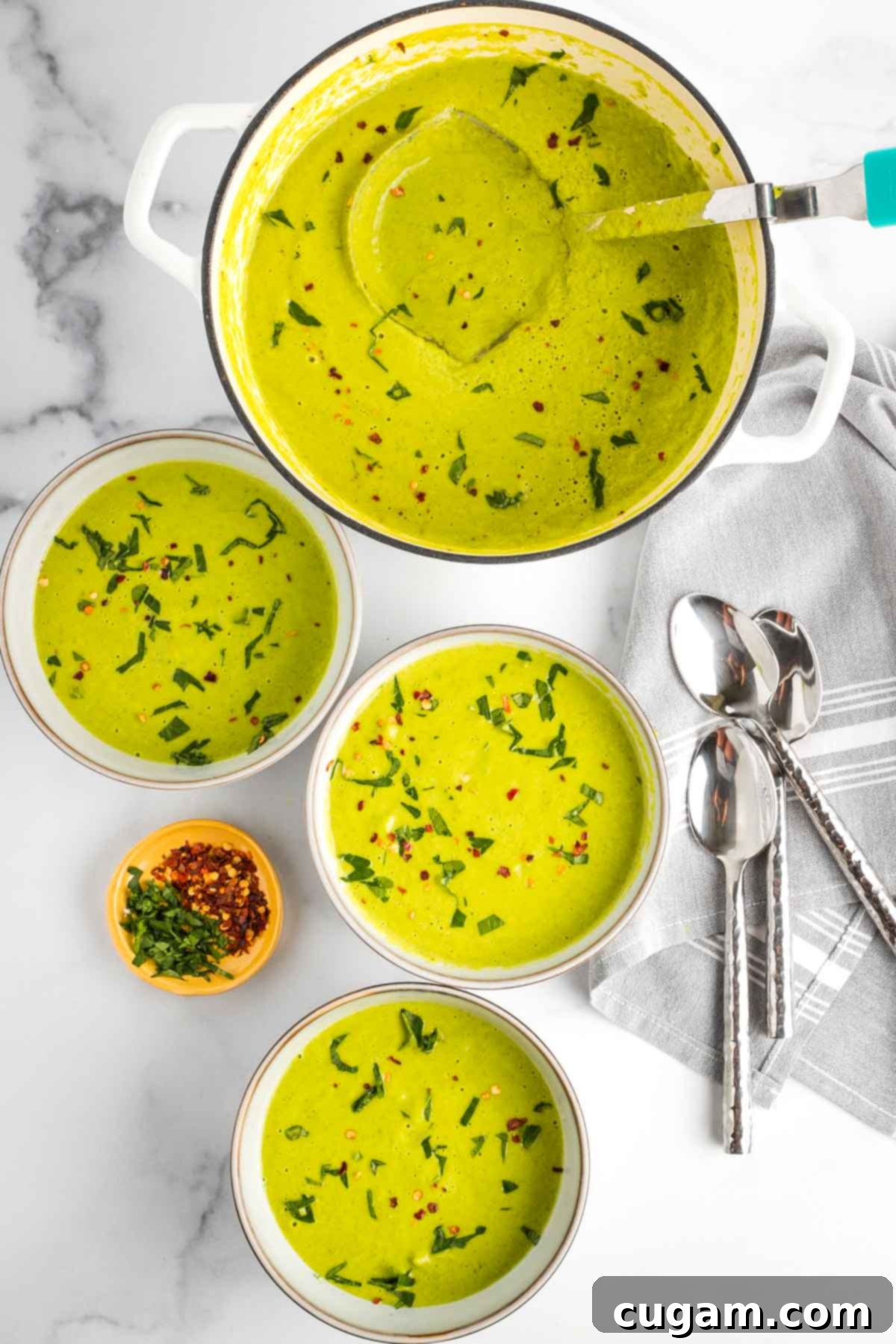 Bowls of bright greenish yellow soup with fresh herbs and crushed red pepper on top plus a pot of same.