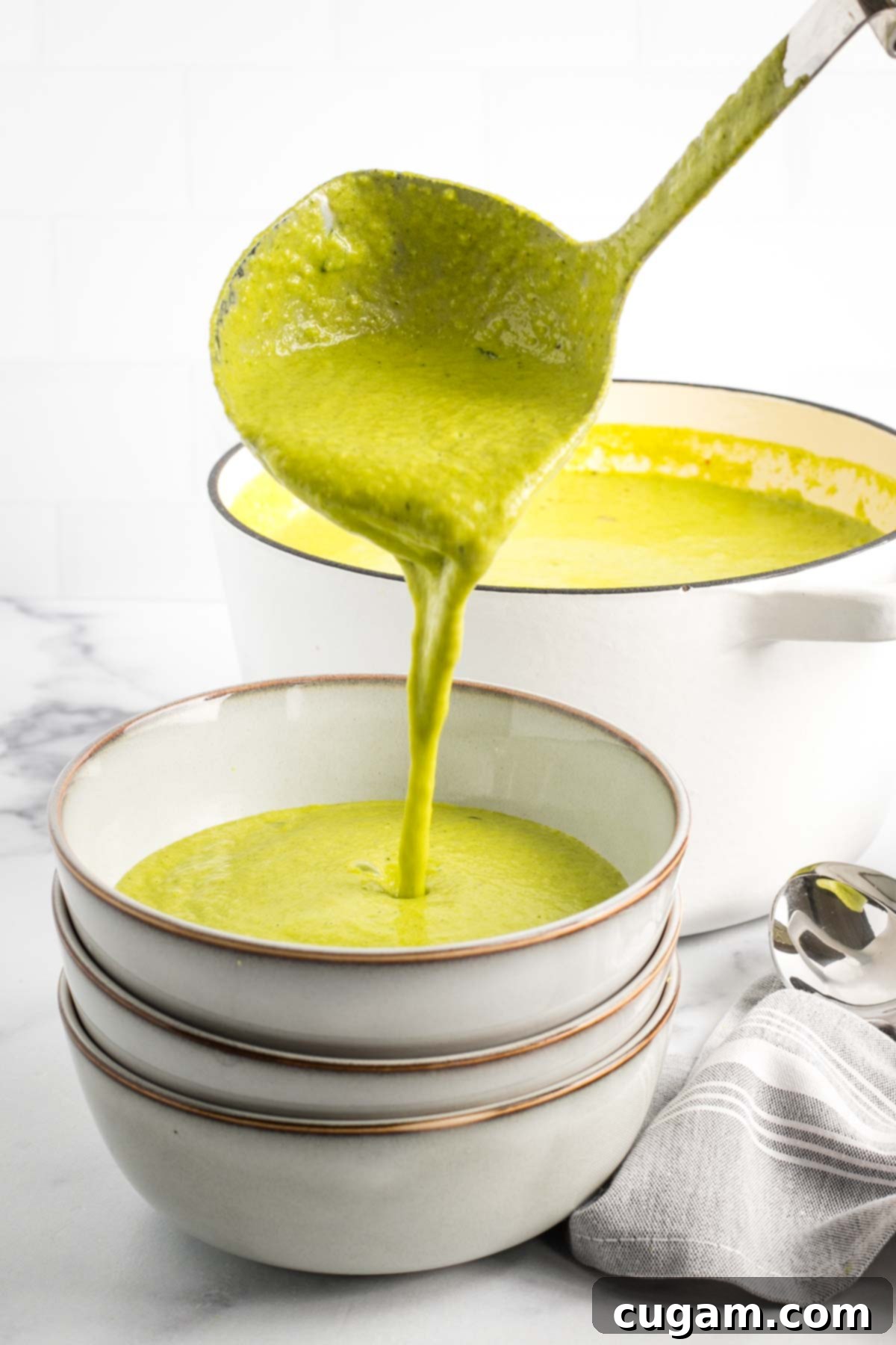 Ladling thick green soup from a dutch oven into bowls.
