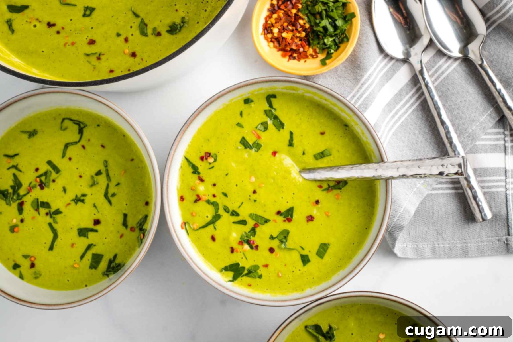Bowls of creamy pureed vegetable soup, garnished with fresh herbs and crushed red pepper.