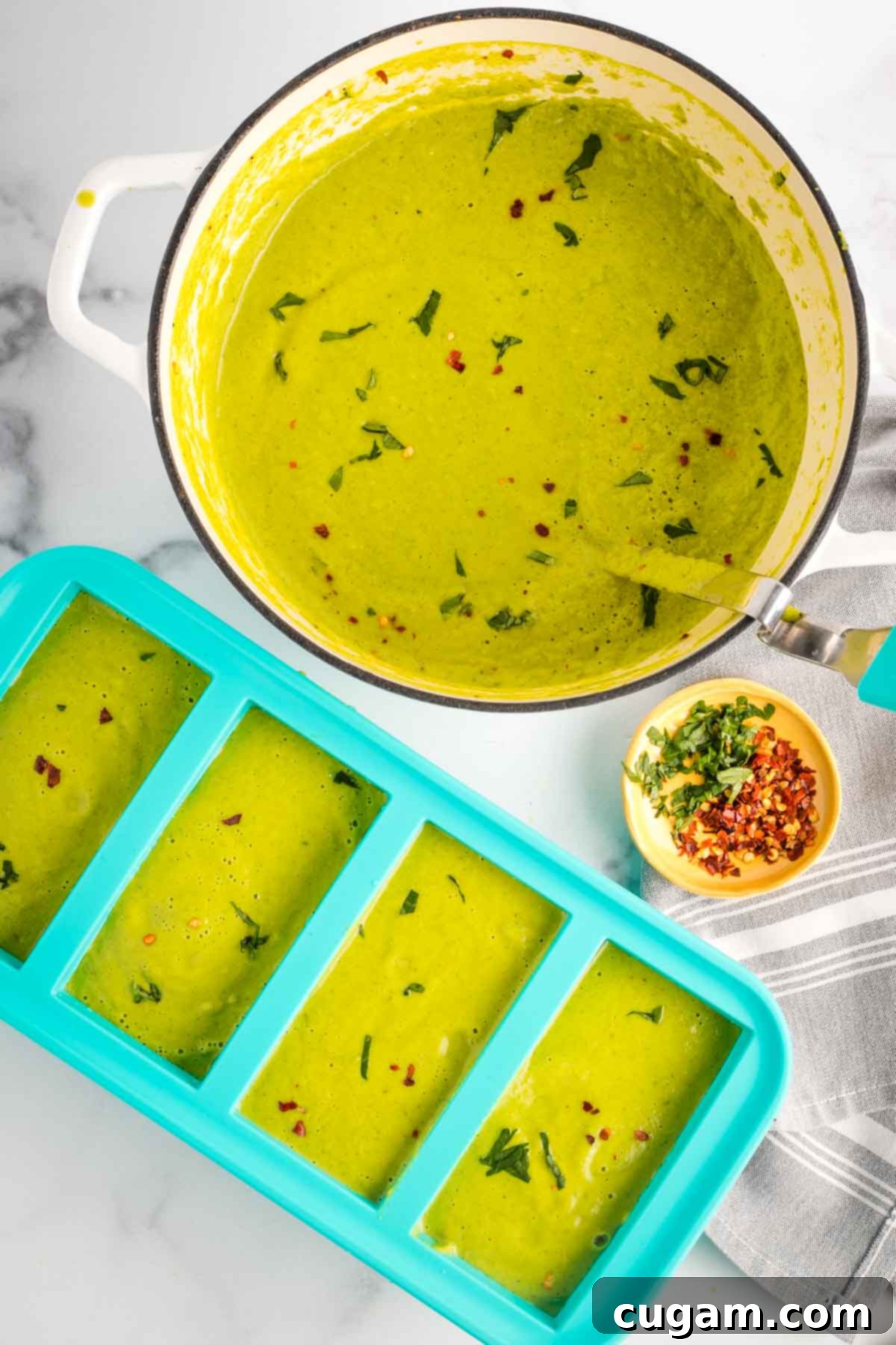 Pot of green pureed vegetable soup and a ladle, transferring soup to souper cubes for freezing.