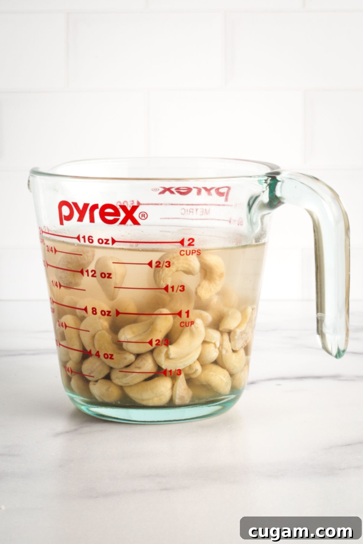Cashews covered in water in a glass measuring cup.