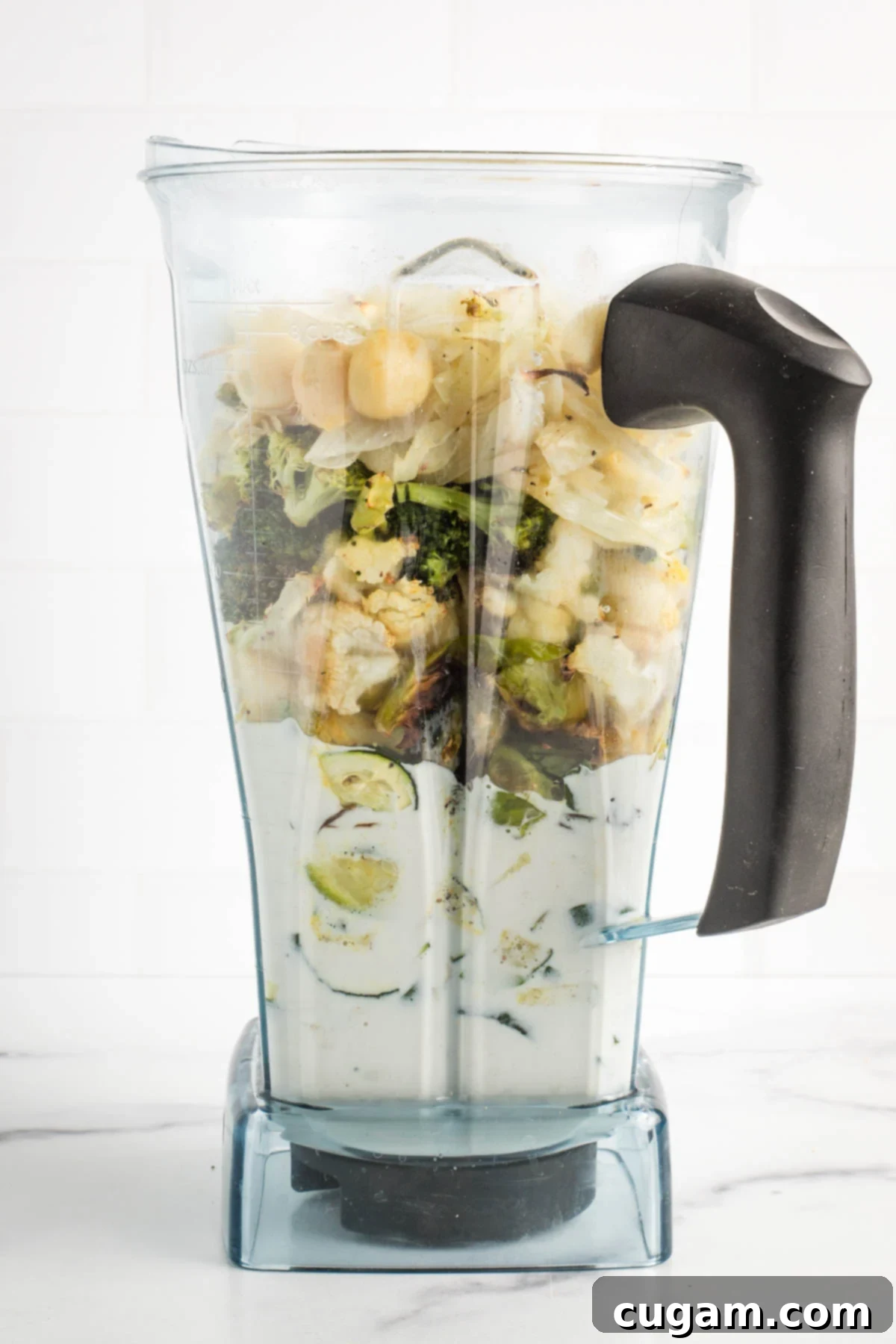 Cashew cream and roasted vegetables in the pitcher of a blender.