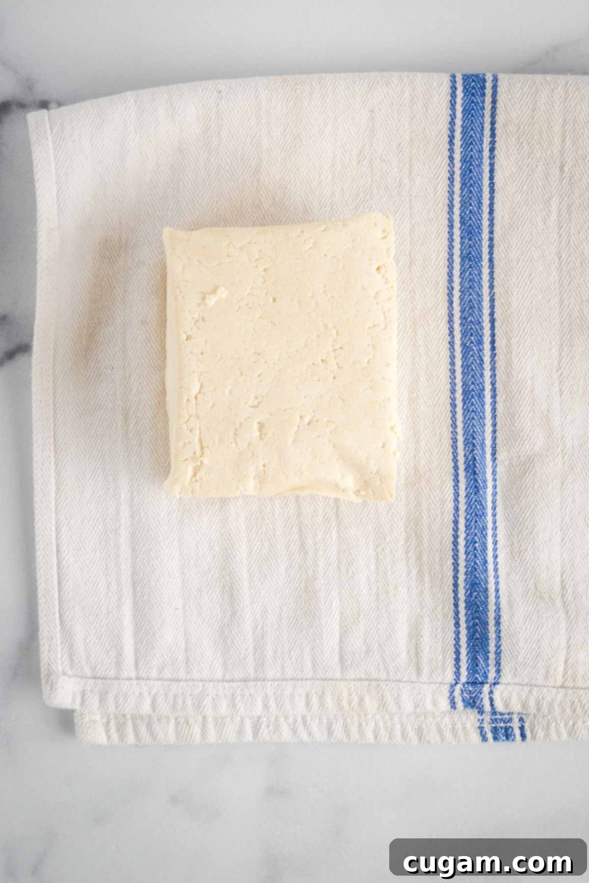 Block of drained firm tofu on a clean dish cloth.