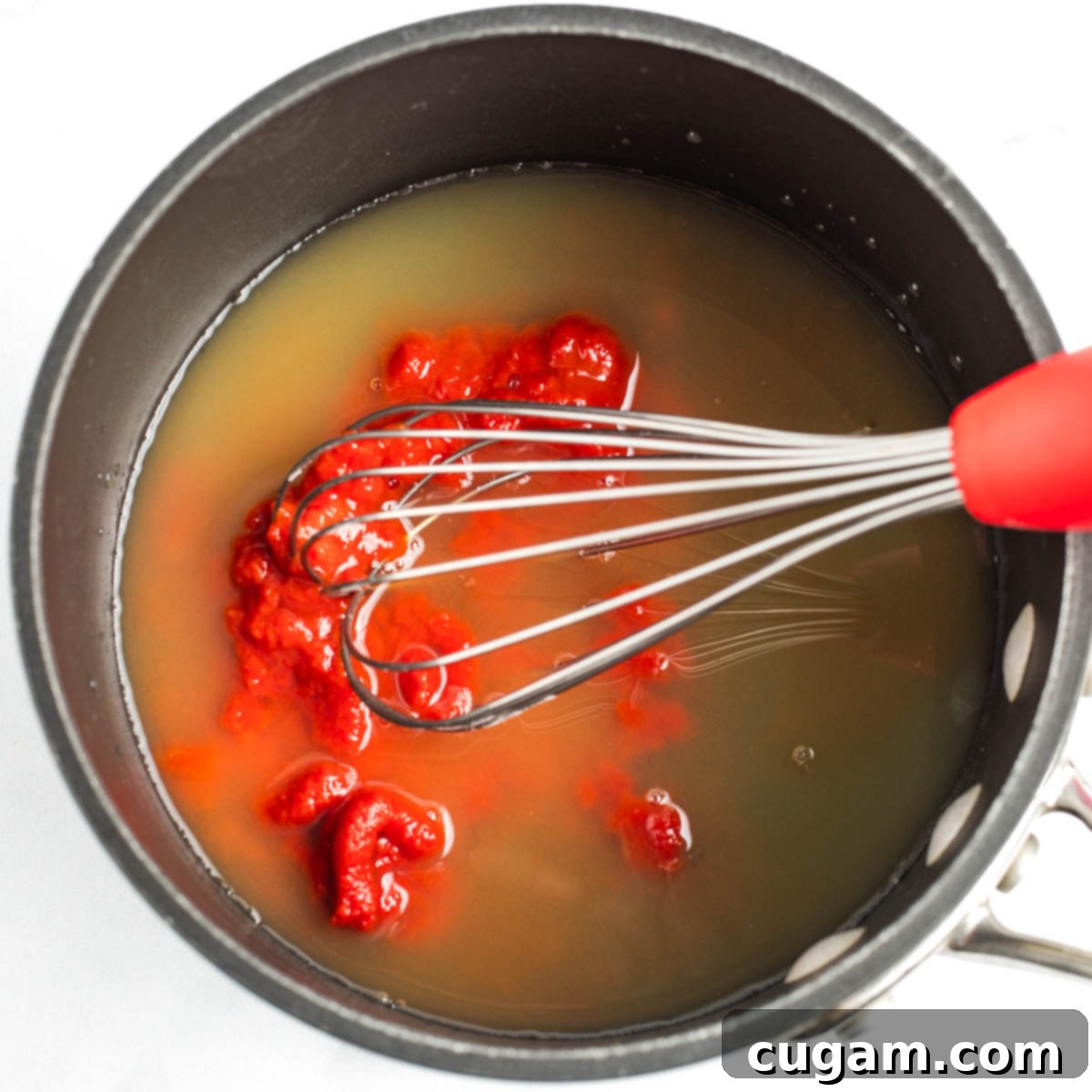 Whisking tomato paste into pineapple juice, vinegar and maple syrup.