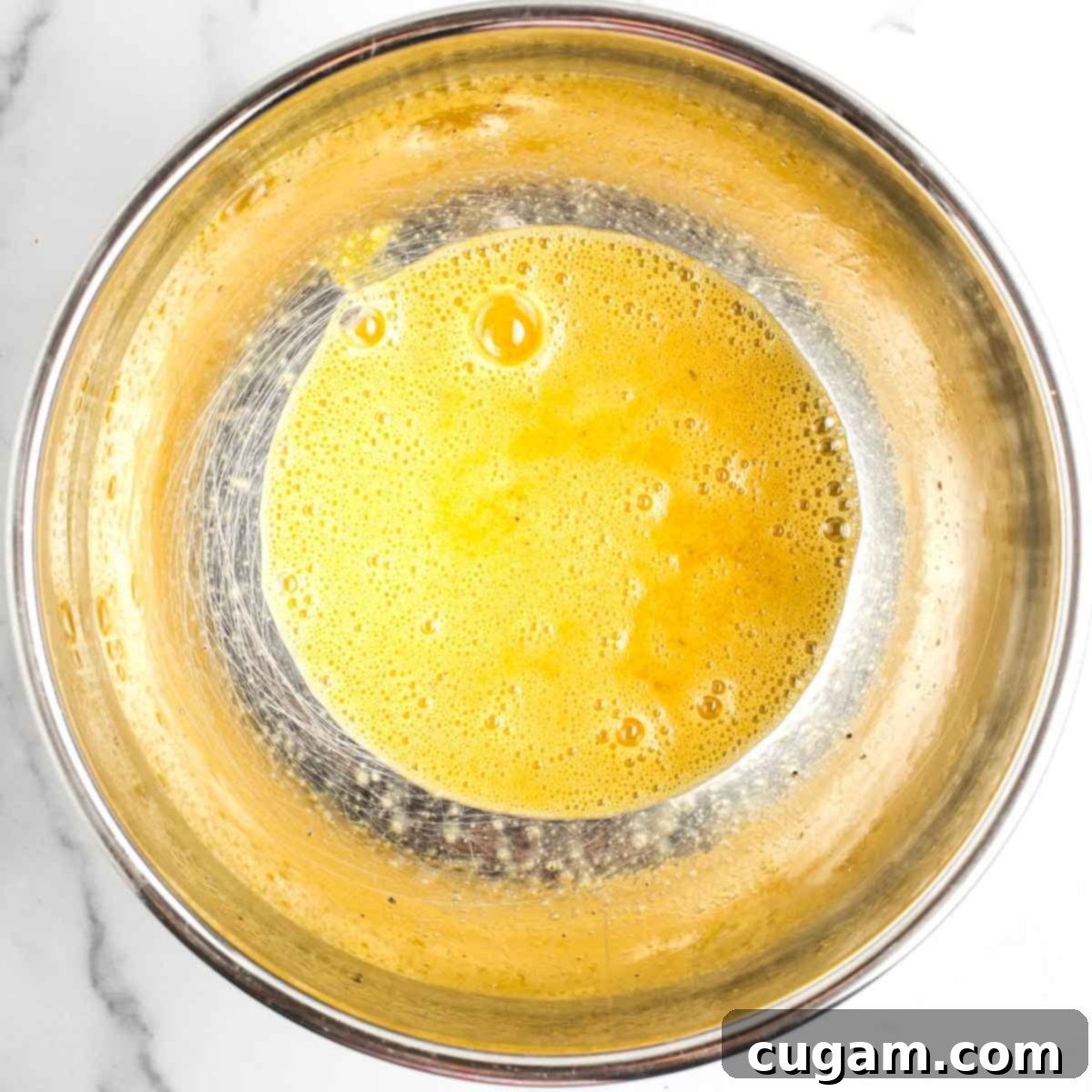 Bowl with bubbly, whisked eggs plus salt and pepper. The mixture is light yellow and well-combined, ready for the sweet potatoes.