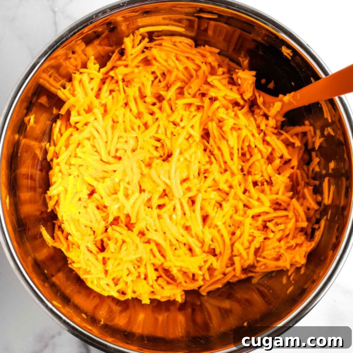 Shredded sweet potatoes in a bowl on top of whisked eggs. The bright orange strands of sweet potato are ready to be mixed with the yellow egg base.