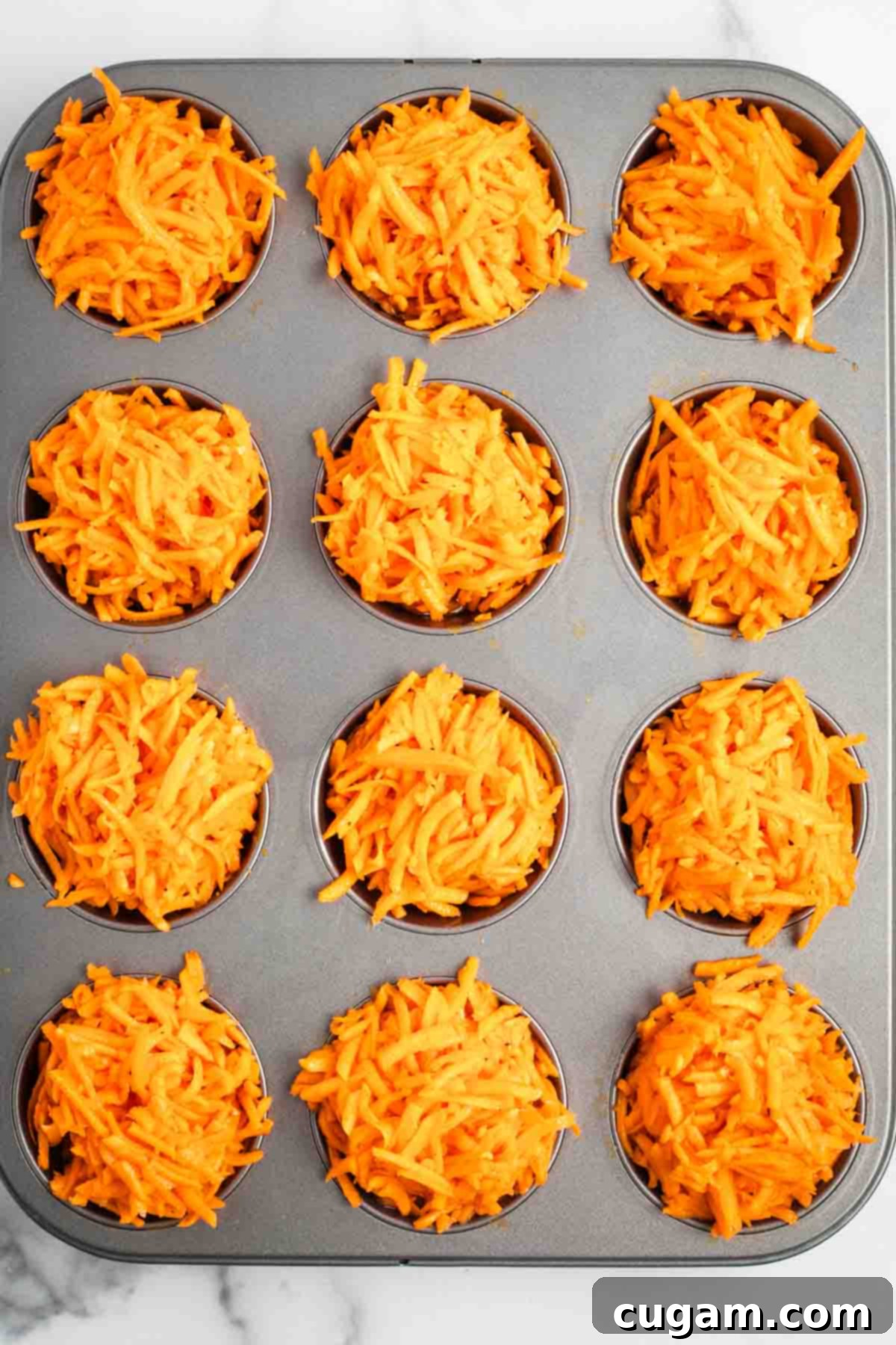 Muffin tins filled with shredded sweet potato and egg mixture, ready to be baked. Each cup is slightly mounded, anticipating shrinkage during cooking.