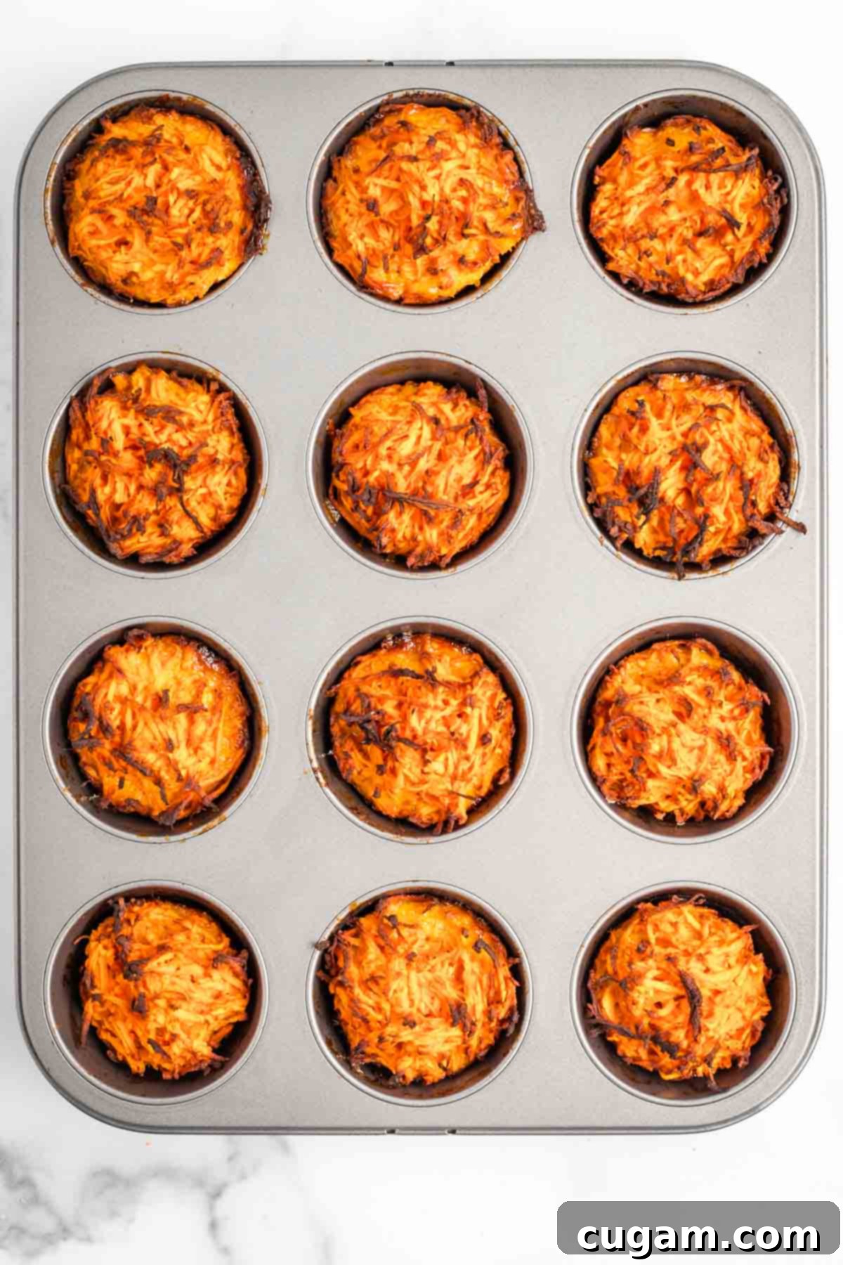 Muffin tins filled with baked and crisped sweet potato and egg mixture. The kugel cups are golden brown and firm, indicating they are fully cooked and ready to be served.