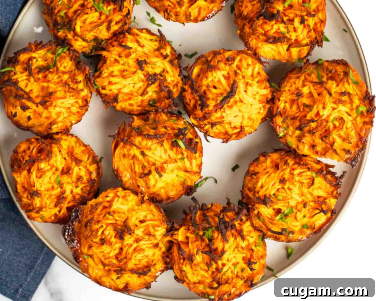 A close-up of Debra Klein, the author, smiling and holding a plate of crispy kugel muffins. She looks friendly and approachable, indicating her expertise.