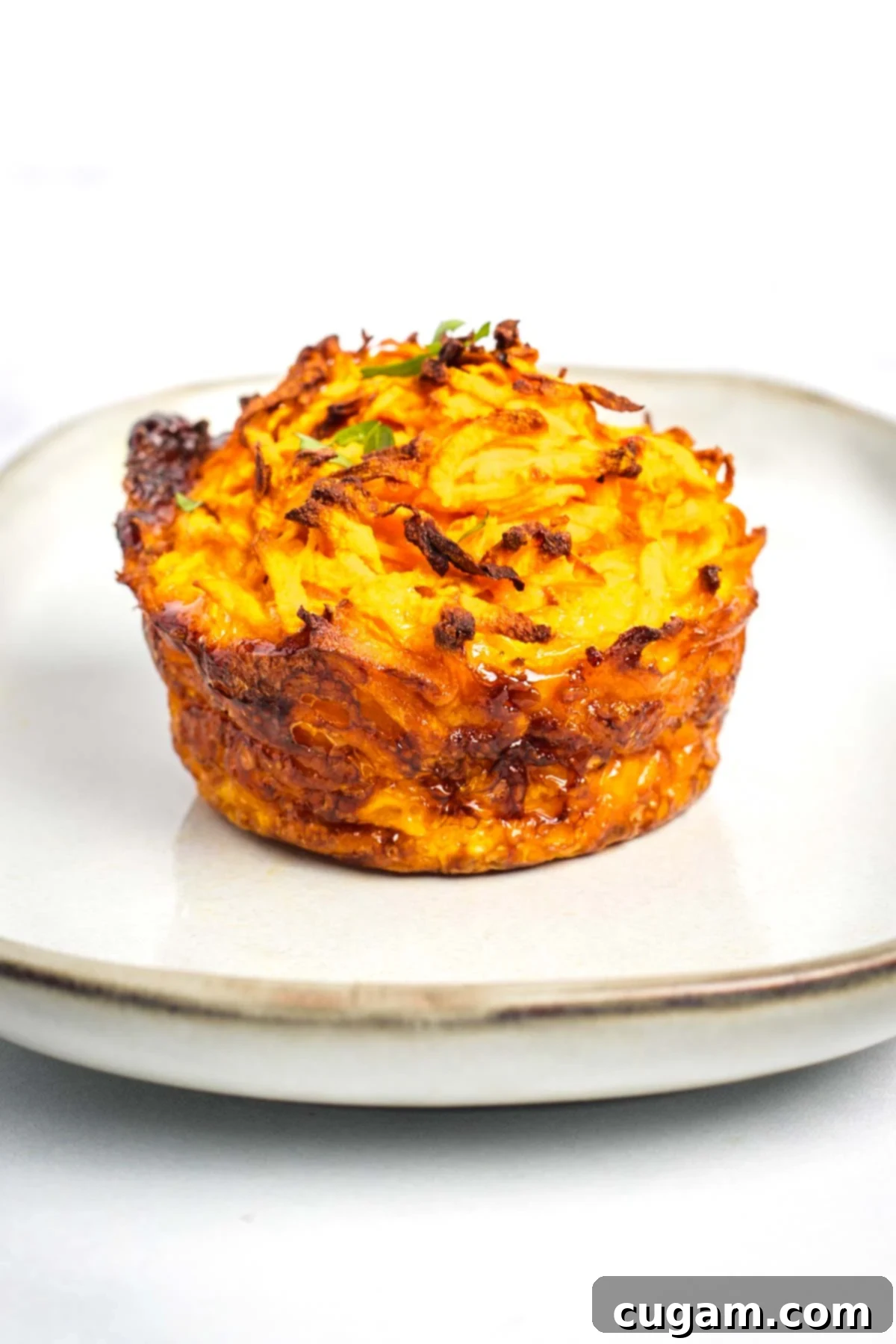 A stack of perfectly baked sweet potato kugel cups, golden-brown and ready to be served, resting on a rustic cutting board. Some fresh herbs are scattered around for garnish, suggesting a fresh and comforting dish.