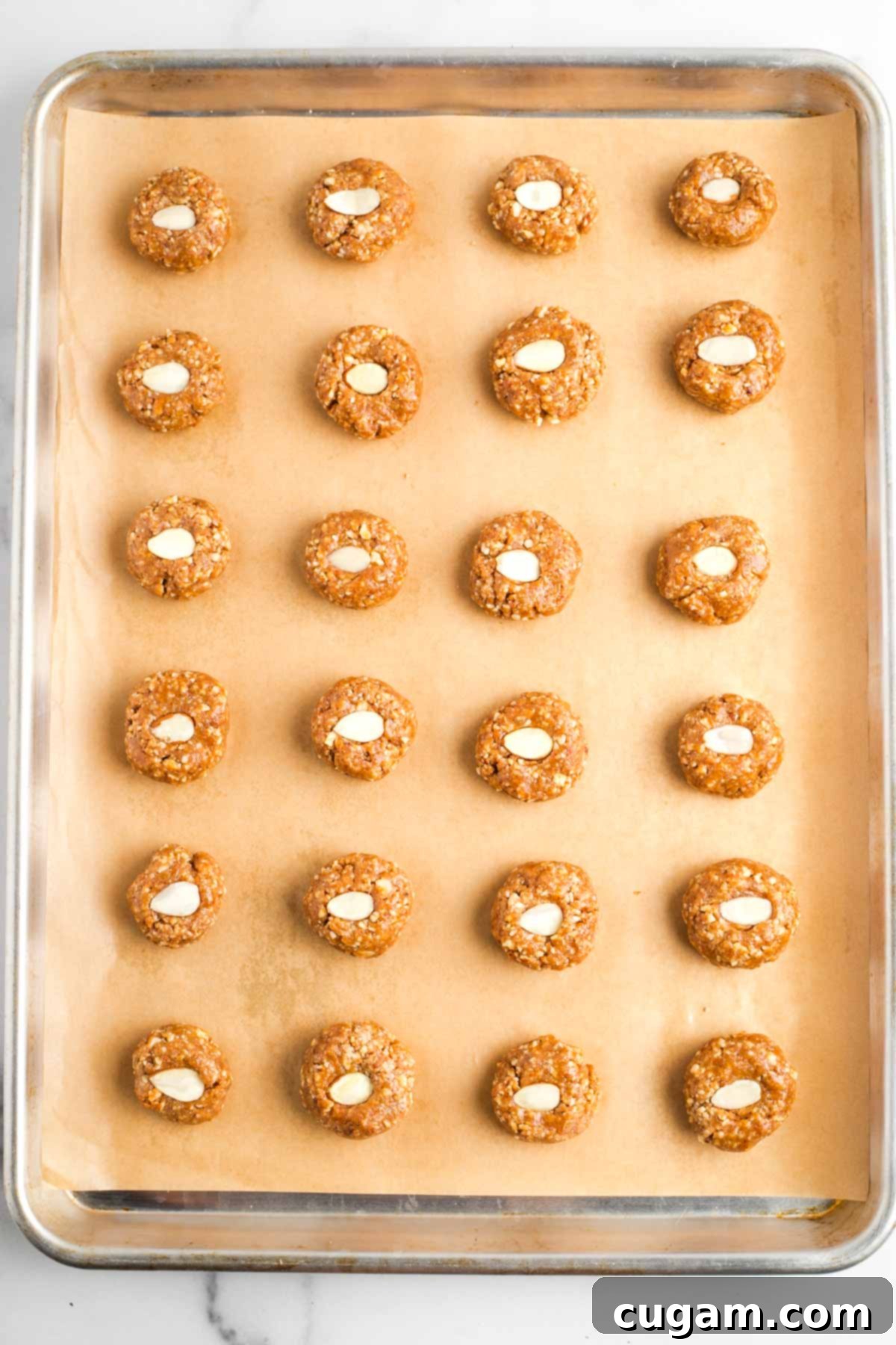 Decadent Vegan Almond Macaroons Enrobed in Chocolate 13 Almond cookies, with a decorative almond slice in the center, lined up on a baking sheet, ready to bake.