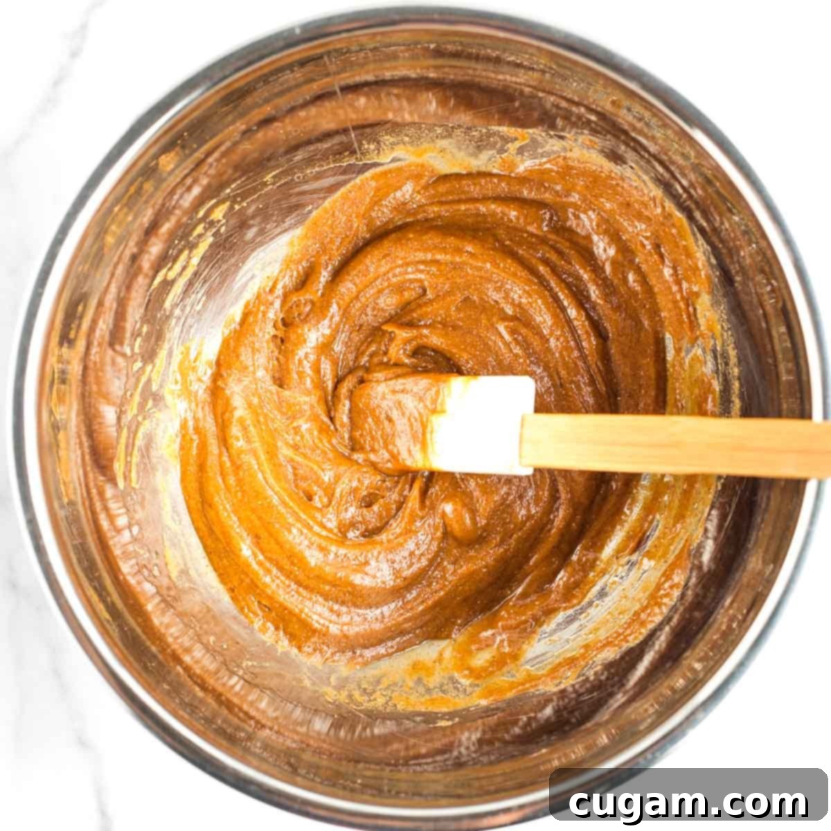 A spatula mixing wet ingredients for almond macaroons in a bowl until smooth.