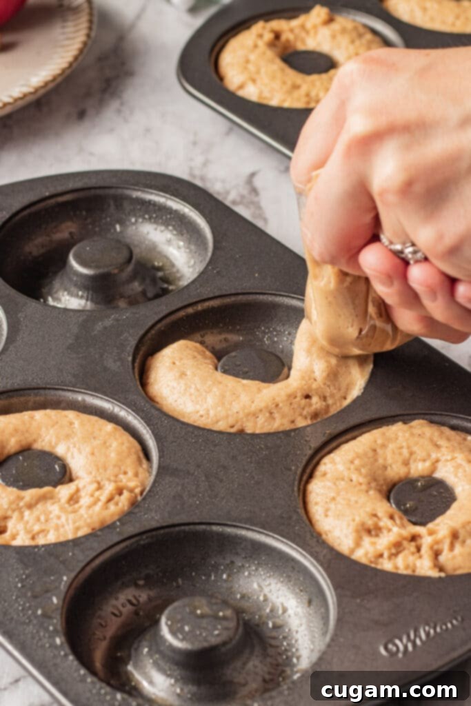 Apple cider donut batter being piped into a donut pan. 