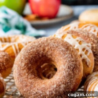 Baked apple cider donut on wire rack and metal pan with other baked donuts.