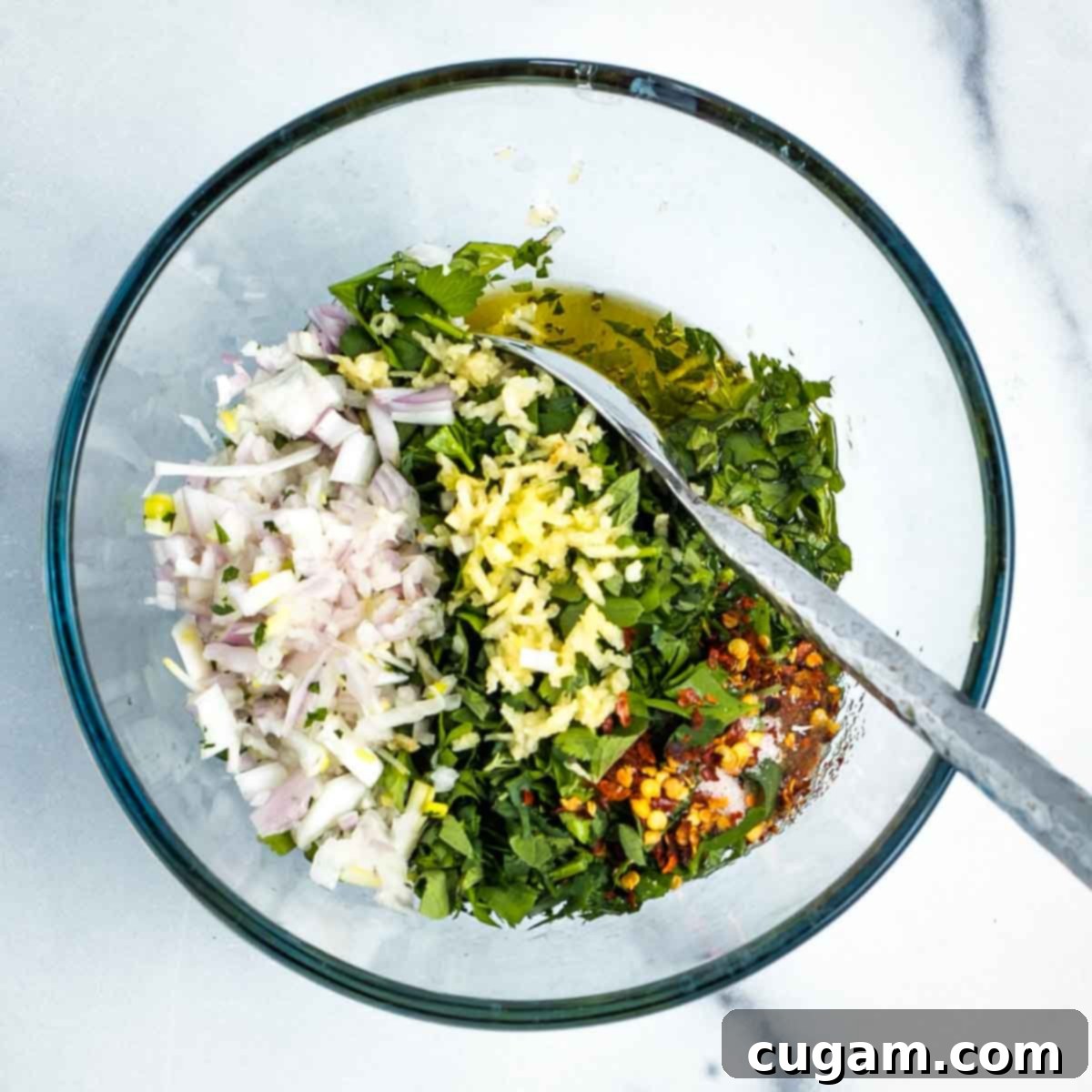 Small glass mixing bowl with chopped fresh herbs, garlic, shallot, spices, olive oil, and red wine vinegar, ready to be mixed.