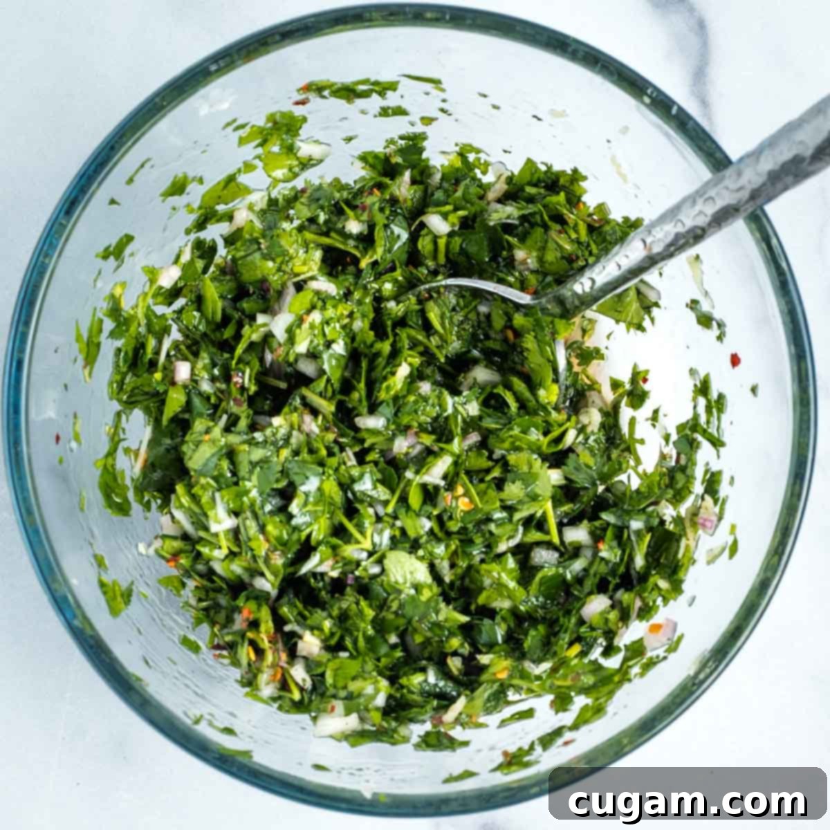 Fresh and vibrant green chimichurri sauce, with flecks of crushed red pepper, pink shallots, and grated garlic, mixed well in a bowl.