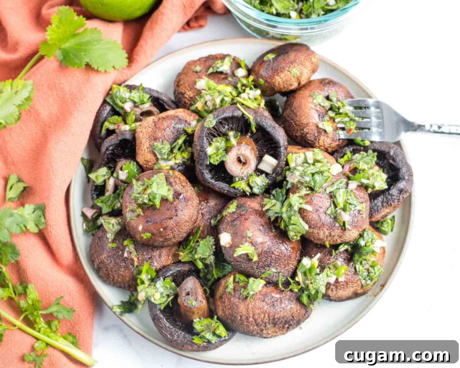 Roasted portobello mushrooms in a bowl, being generously spooned with bright green chimichurri sauce.
