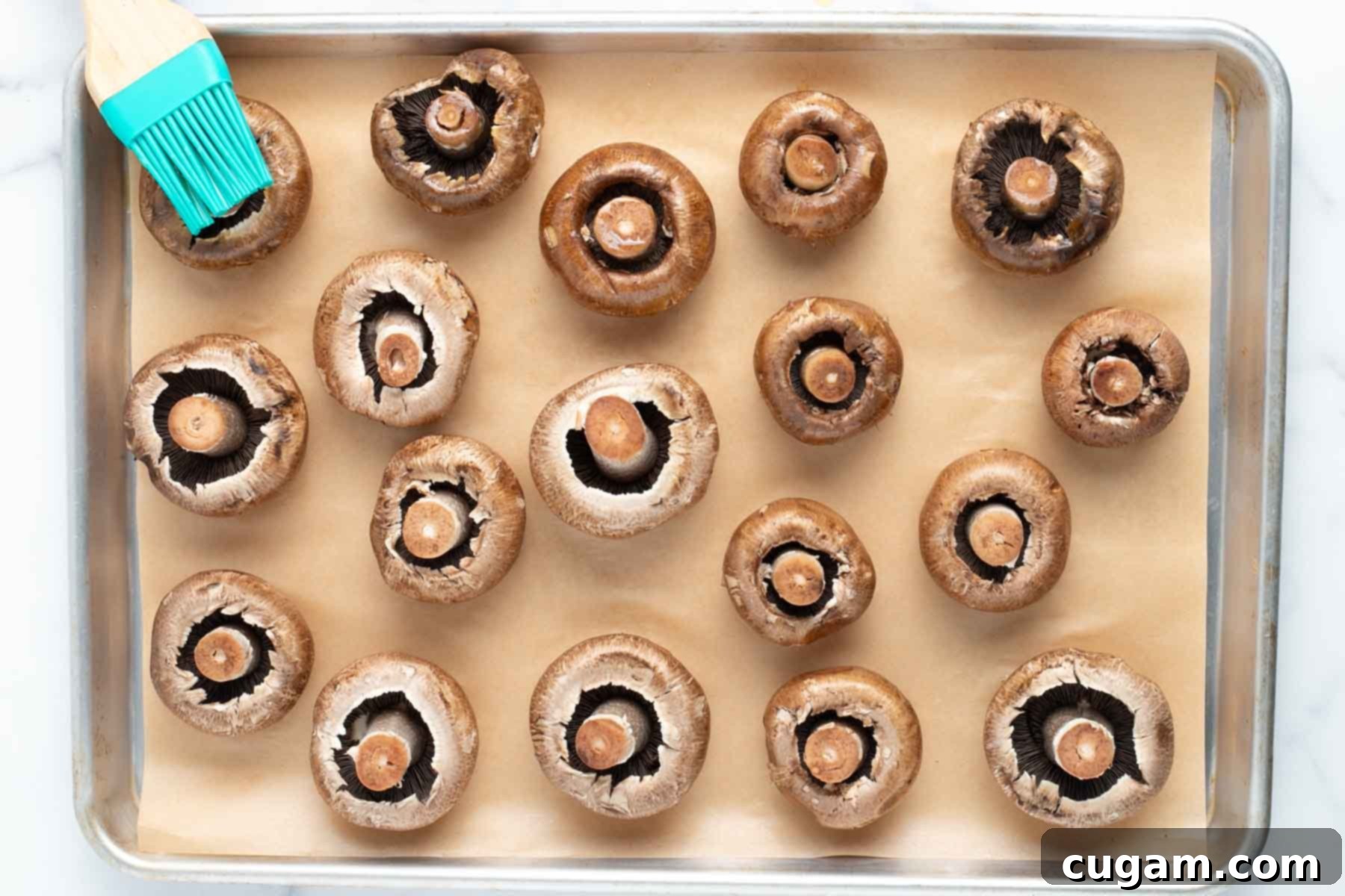 Portobello mushrooms, stem side up on a baking tray lined with parchment, being brushed with olive oil.