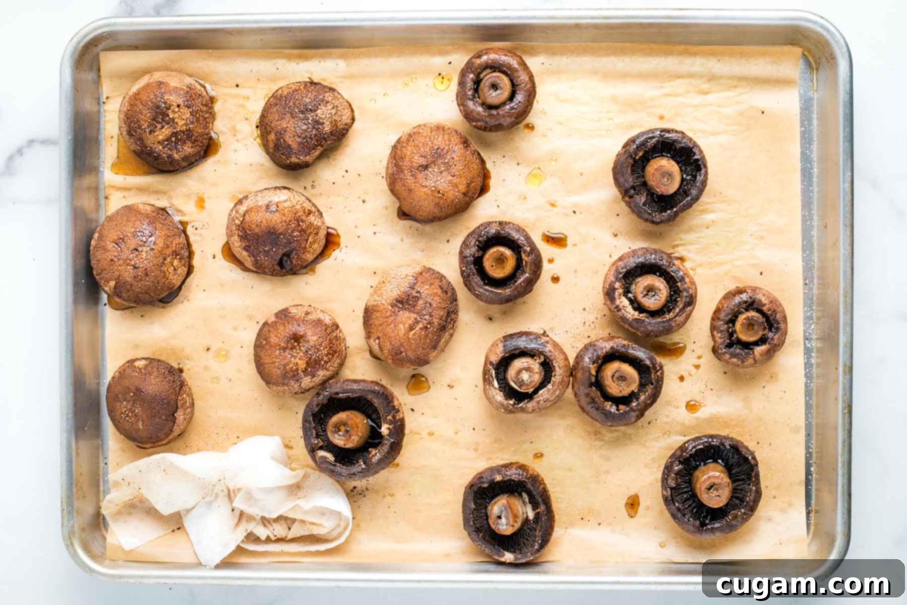 Roasted mushrooms on a tray, cooked, half turned onto stems, half showing stems with a paper towel, absorbing the liquid.