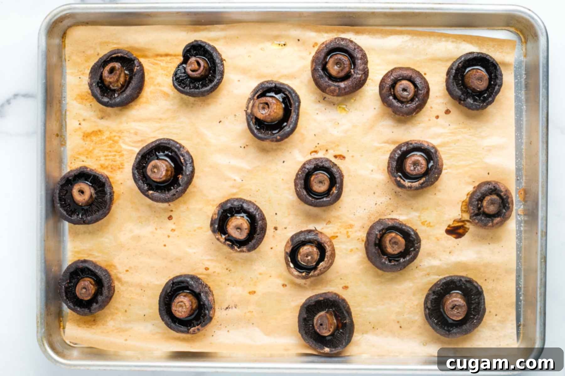 Portobello mushrooms on a baking tray, stem side up, showing mushroom liquid collected in the caps.