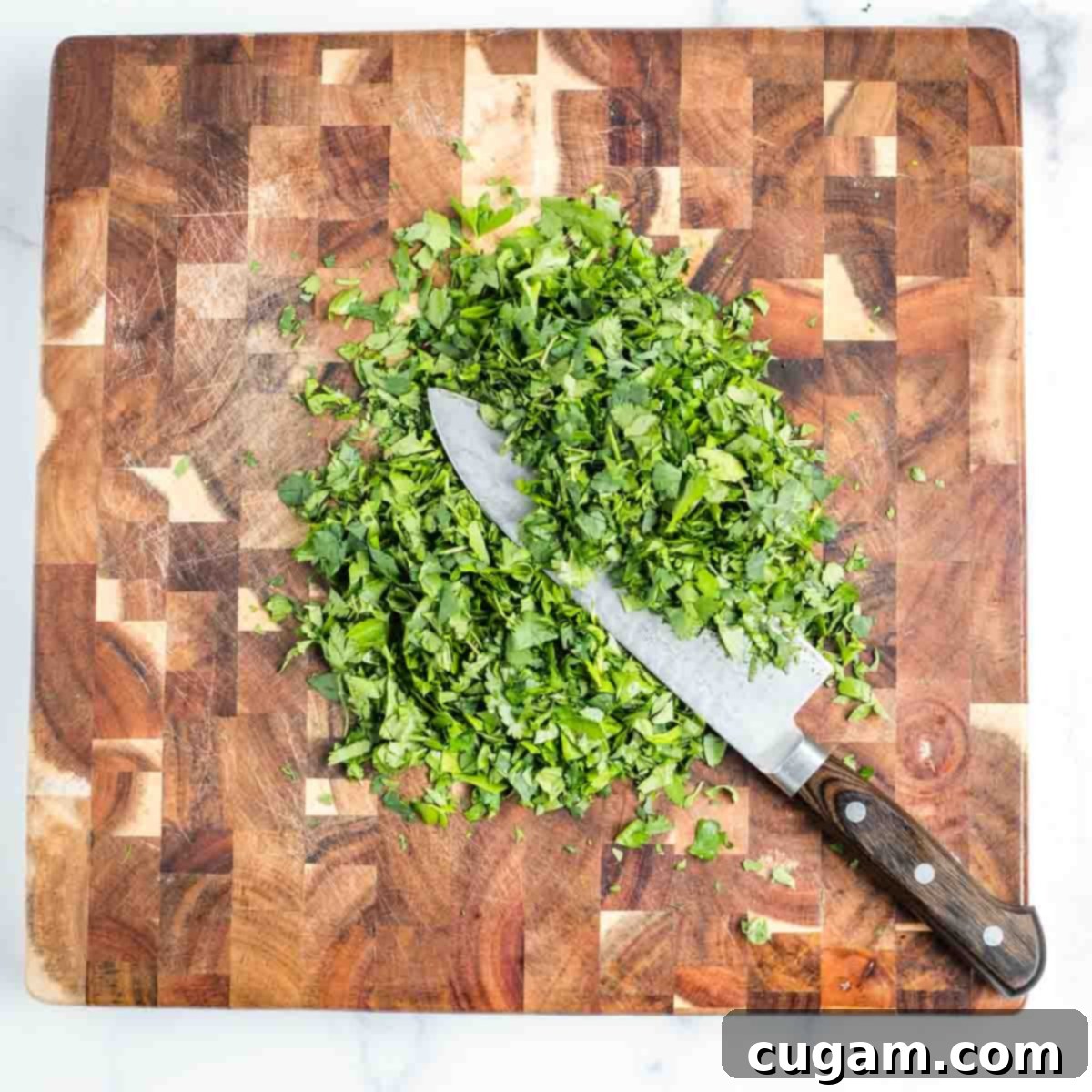 Chef's knife finely chopping a pile of fresh herbs like parsley and cilantro.