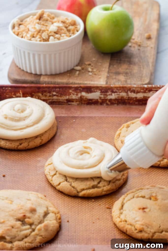 Piping frosting onto baked caramel apple cookies on baking sheet. 
